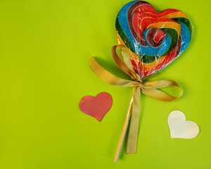 On a green background lies a packaged large multi-colored heart-shaped lollipop. copy space....