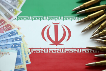 Many bullets and iranian rials money bills on flag of Islamic Republic of Iran close up