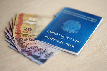 Brazilian work card and social security blue book and reais money bills close up