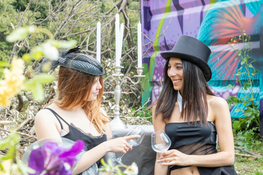 Groupe multiethnique et multiracial de femmes en tenue vintage élégante avec chapeau haut de forme et bibi à voilette noirs, pique nique urbex trinquant, fête des vendanges, beaujolais nouveau