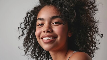 Close up studio shot of beautiful young mixed race woman model with curly dark hair looking at camera with charming cute smile while posing against white blank copy space wall for your content 
