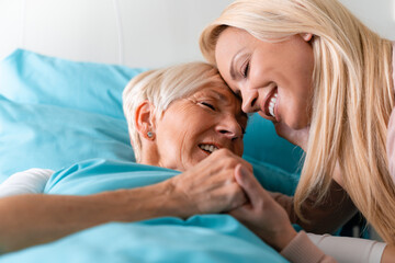 Adult daughter supporting mother in hospital holding hands with eyes closed.