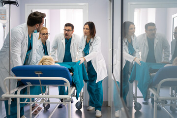 Discussion between medical team while pushing patient into operating room. Surgeons running out of time, wheeling patient into operating theatre. - obrazy, fototapety, plakaty