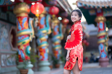 Portrait beautiful cute smiles Asian young woman wearing red traditional Chinese cheongsam decoration and holding a Chinese Fanning for Chinese New Year Festival at Chinese shrine in Thailand