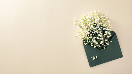 Lilies of the valley in a green postal envelope on a light beige wooden background