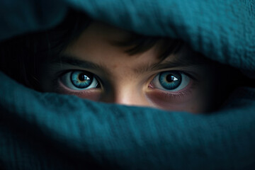 Intense blue eyes of a child peeking through a teal fabric, capturing curiosity and innocence