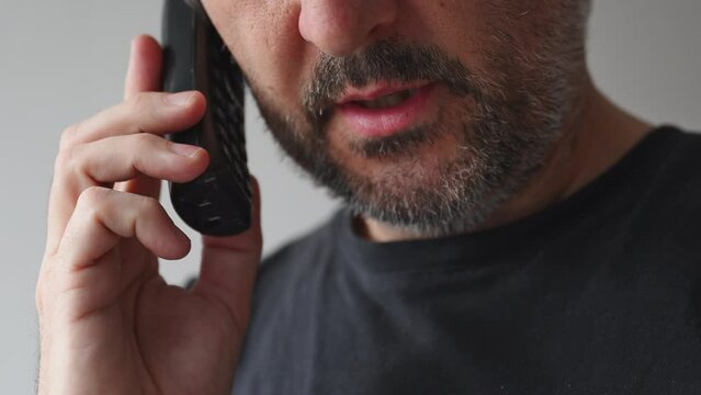 Closeup of adult male talking on cordless landline phone, man during mobile phone conversation indoors