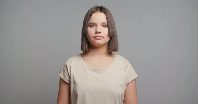 Portrait of young latin teenager female student in beige t-shirt, smiling isolated on gray background. Copy space