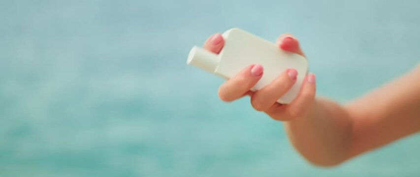 Mineral sunscreen zinc oxide shake well before use. Girl hand holding white tube of skin care cream on ocean sea water background.