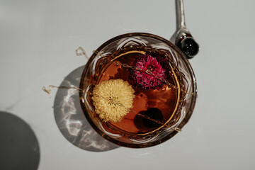 still life, glass of brown liquor on a white background, flowers inside floating, gold chain draped...