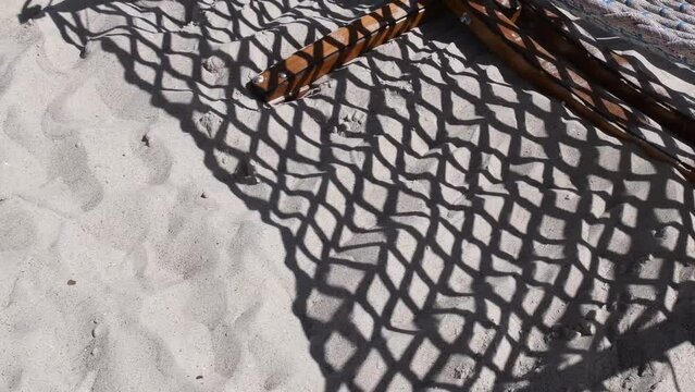 Net pattern shadows of rope hammock swinging above clean beach sand. Silhouette shadows of net knotted hammock. Leisure vacation background