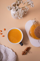Obraz na płótnie Canvas Cup and teapot of sea buckthorn tea and plaid flat lay, top view. Cozy autumn winter time