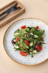 Salad with arugula, cherry tomatoes, cucumbers in a plate on a color background top view, flat lay.