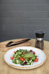 Salad with arugula, cherry tomatoes, cucumbers in a plate on a brick wall background with copy space.