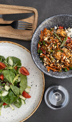 Bowl with tasty rice, meat and vegetables and salad with cherry tomatoes, cucumbers and arugula on dark background
