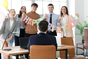 Young man with his colleagues at birthday party in office, back view