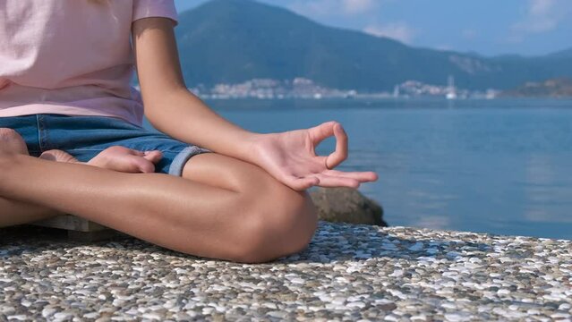 Meditation by the sea. The girl sits on the seashore in a lotus position and meditates.