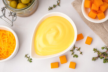 Bowl with tasty cheddar cheese sauce, thyme and olives on white background, closeup
