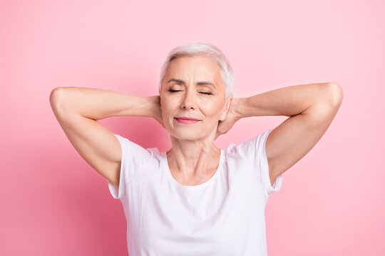 Portrait of relaxed person with white hairdo dressed stylish t-shirt hold hands behind head eyes closed isolated on pink background