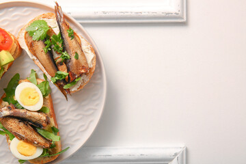 Plate of tasty sandwiches with canned smoked sprats on white wooden background