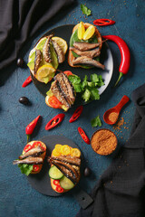 Plate and board of tasty sandwiches with canned smoked sprats on black background
