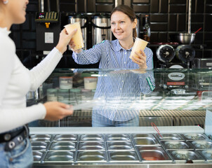 Smiling friendly saleswoman standing behind glass counter with large selection of flavorful...
