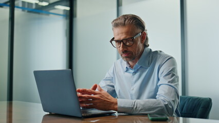 Focused businessman calling laptop at conference room. Eyeglasses man talking