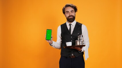 Bearded waiter presents greenscreen on phone display, holding smartphone to show isolated mockup...