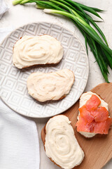 Tasty sandwiches with cream cheese and fish on light background