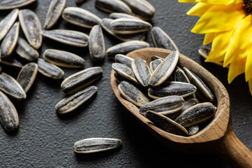Pile of black roasted salty sunflower seeds with flower on rustic table, nut concept, Helianthus annuus