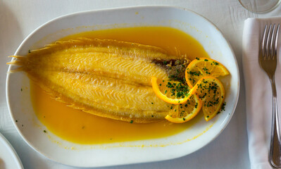 Appetizing black sole fish in orange dipping sauce garnished with orange slices and greens