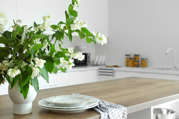 Vase with blooming jasmine flowers on wooden table in modern kitchen