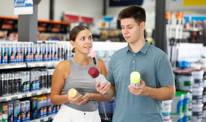 Positive man and woman choosing paint in aerosol at local hardware store