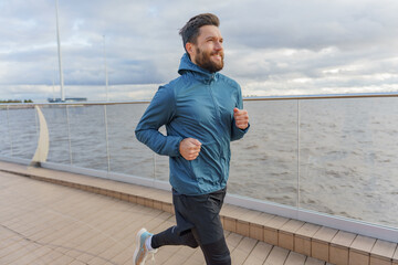 Fototapeta premium Focused man in sportswear running along the waterfront, with urban skyline in the background