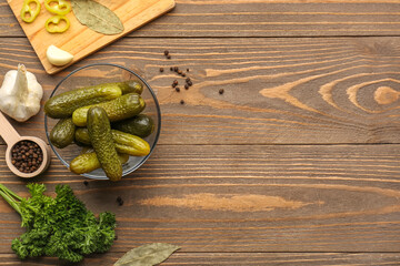Glass bowl with pickled cucumbers and different spices on wooden background - obrazy, fototapety, plakaty