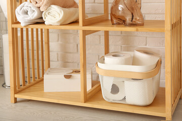 Wooden shelving unit with toilet paper rolls, clean towels and decor near light brick wall, closeup