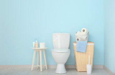 Ceramic toilet bowl, basket with paper rolls and cosmetic products near color wall