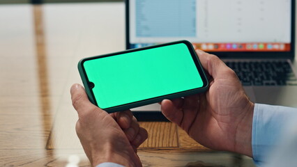 Businessman arms holding mockup smartphone indoors. Boss using green display