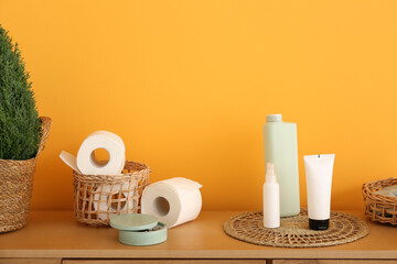 Basket with toilet paper rolls and cosmetic products on wooden table near color wall