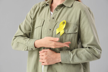 Woman with yellow awareness ribbon on light background, closeup