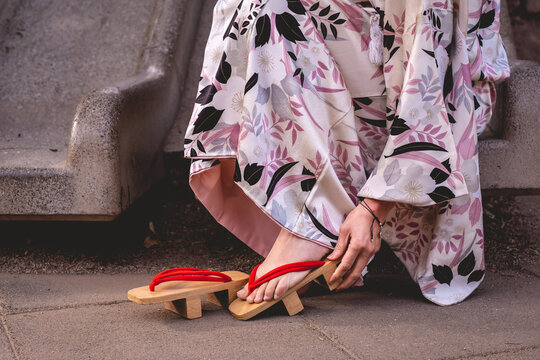 Japanese beauty, elegance and tradition: beautiful japanese model in traditional white silk kimono with pink leaves design and 'geta' wooden sandals in a urban park