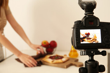 Woman making tasty apple pie on display of professional photo camera in studio - obrazy, fototapety, plakaty