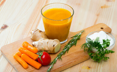 Glass of fresh carrot juice with grated ginger on wooden board