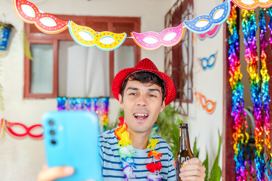 Joyful young Brazilian celebrating Carnival, snapping a selfie with his smartphone for social media. He is holding a beer bottle.