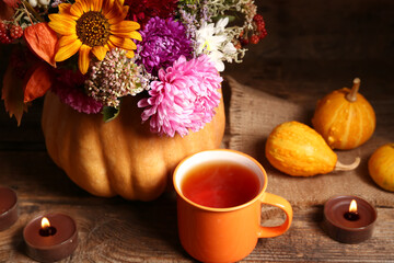 Beautiful autumn bouquet in pumpkin with burning candles and cup of tea on wooden background