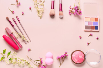 Frame made of makeup brushes, cosmetic products and flowers on pink background