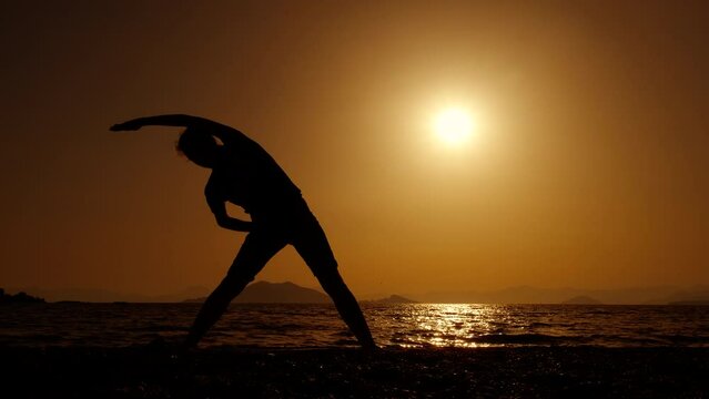 Woman doing stretching exercises against dusk. A view of woman silhouette stretching her back and enjoy sport on the nightfall sky in summer.