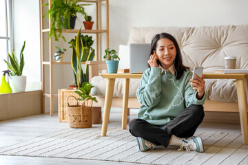 Young Asian woman with earphones and mobile phone at home