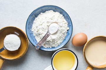 mise en place of ingredients for making vanilla almond muffins, top view of sugar, eggs, oil, flour milk on a marble table, process of making vanilla almond muffins
