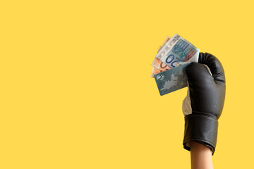 Female hand in boxing glove with money on yellow background